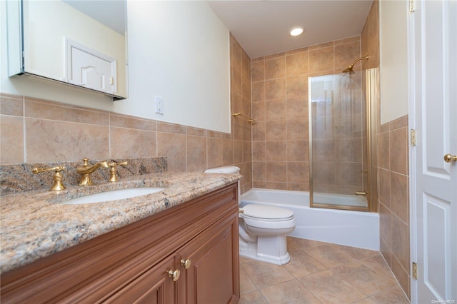 full bathroom with tile patterned flooring, bath / shower combo with glass door, toilet, vanity, and tile walls