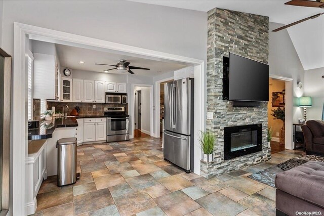 living room with high vaulted ceiling, a stone fireplace, ceiling fan, and sink