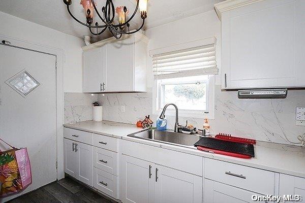 kitchen with sink, dark wood-type flooring, tasteful backsplash, a chandelier, and white cabinets