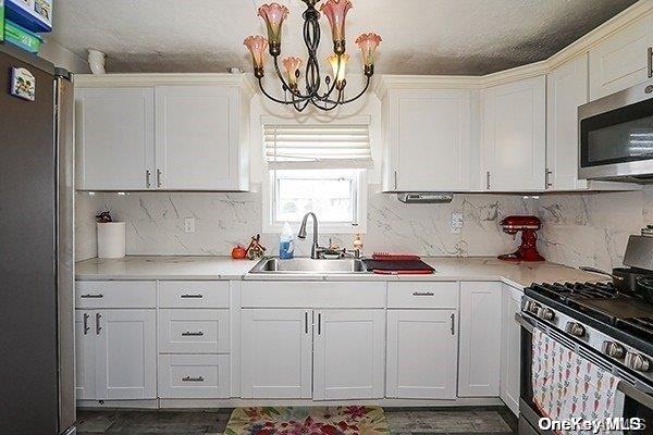 kitchen featuring appliances with stainless steel finishes, a textured ceiling, sink, a notable chandelier, and white cabinetry