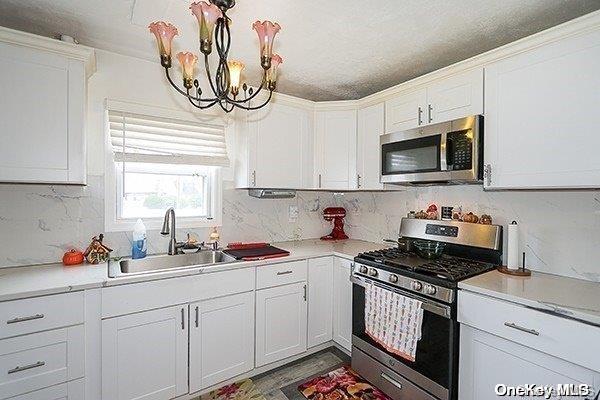 kitchen with sink, white cabinets, a notable chandelier, and appliances with stainless steel finishes