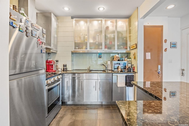 kitchen with sink, stainless steel appliances, dark stone countertops, decorative backsplash, and dark tile patterned flooring