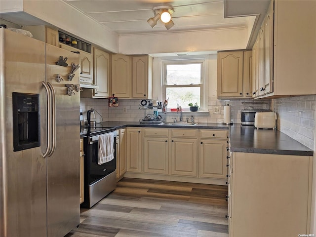 kitchen featuring dark countertops, tasteful backsplash, under cabinet range hood, stainless steel appliances, and a sink