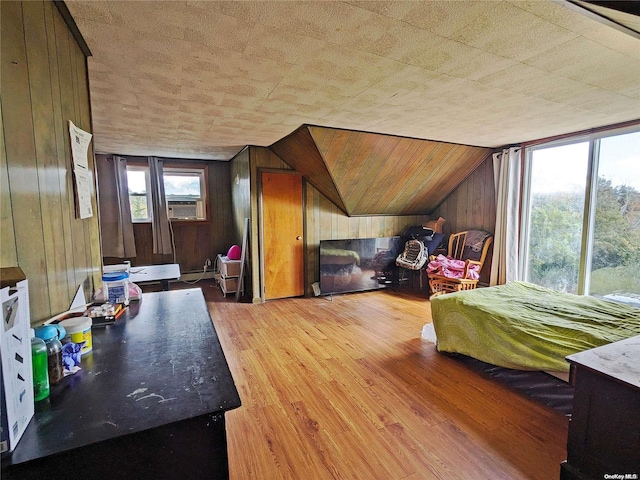 bedroom with baseboard heating, light wood-style flooring, lofted ceiling, and wood walls