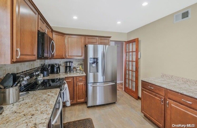 kitchen with appliances with stainless steel finishes, french doors, tasteful backsplash, light stone counters, and light hardwood / wood-style floors