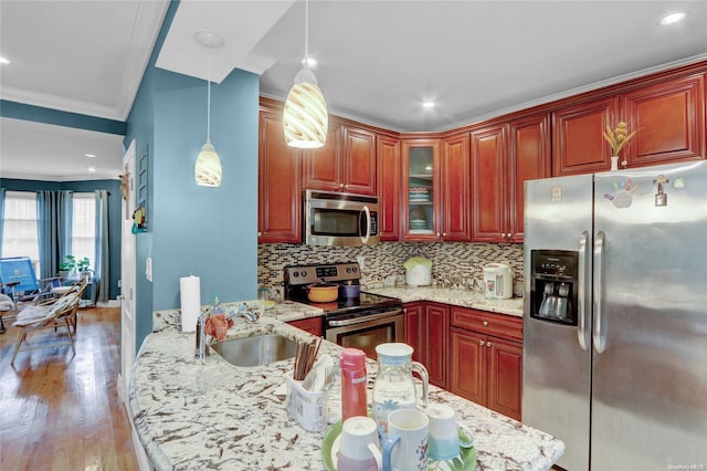 kitchen with light wood-type flooring, light stone counters, stainless steel appliances, sink, and decorative light fixtures