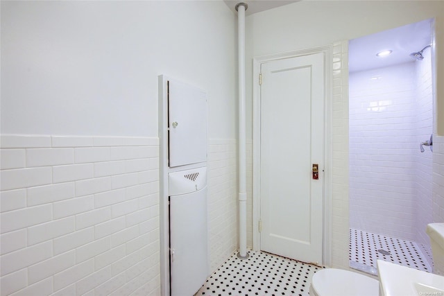 bathroom with toilet, a tile shower, and tile walls