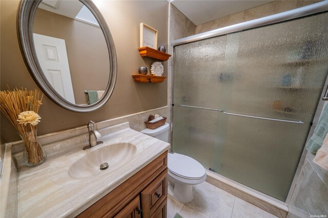 bathroom with tile patterned floors, a shower with door, vanity, and toilet