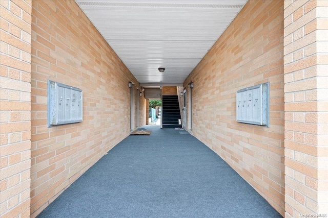 hall featuring dark carpet and brick wall