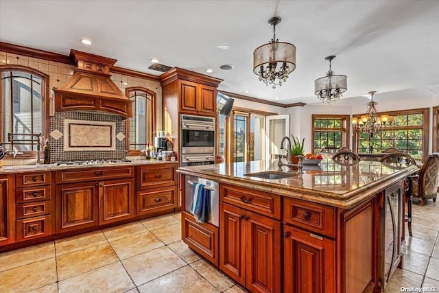 kitchen featuring sink, an inviting chandelier, pendant lighting, a kitchen island with sink, and custom exhaust hood