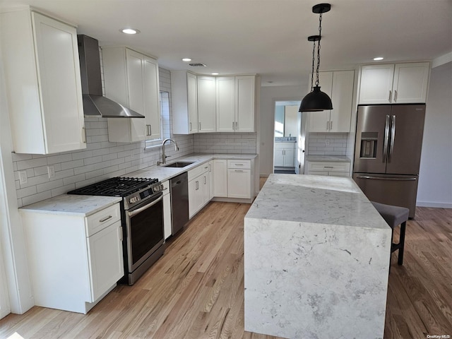 kitchen with pendant lighting, white cabinets, wall chimney range hood, sink, and stainless steel appliances