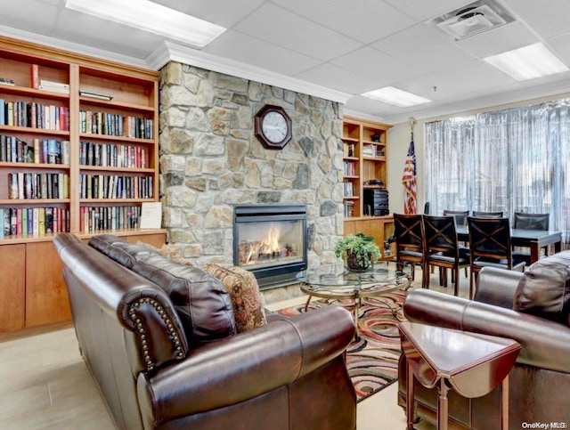 living room featuring a fireplace, crown molding, a drop ceiling, and built in features