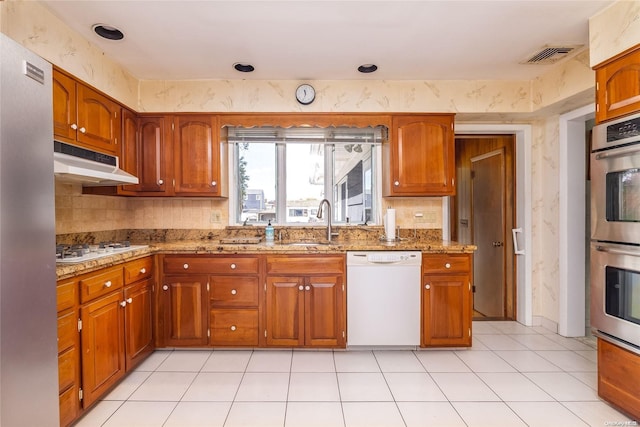 kitchen featuring light tile patterned floors, stainless steel appliances, light stone counters, and sink