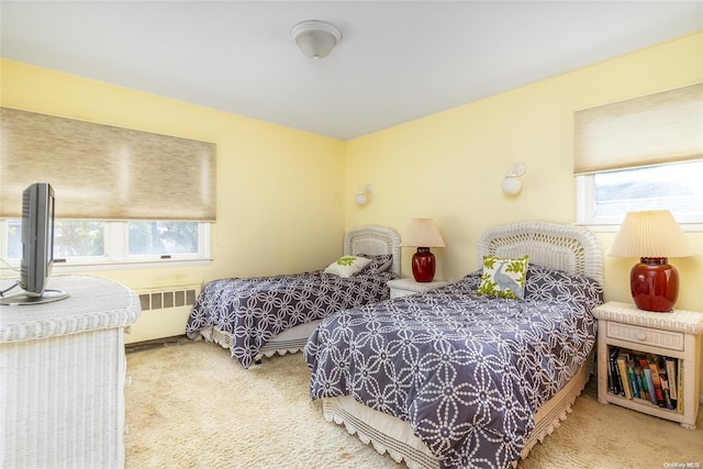 bedroom featuring light carpet, radiator heating unit, and multiple windows