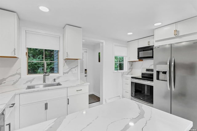 kitchen featuring light stone countertops, backsplash, stainless steel appliances, sink, and white cabinetry