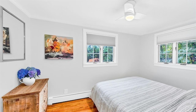 bedroom with multiple windows, light wood-type flooring, baseboard heating, and ceiling fan