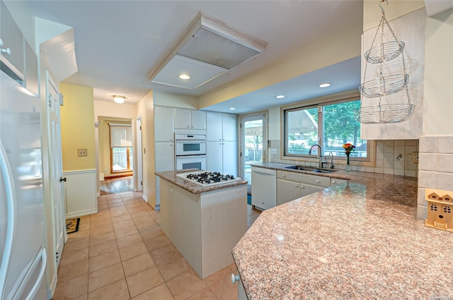 kitchen featuring backsplash, white appliances, sink, a kitchen island, and light tile patterned flooring