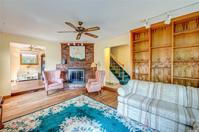 living room with hardwood / wood-style floors, rail lighting, a brick fireplace, and ceiling fan