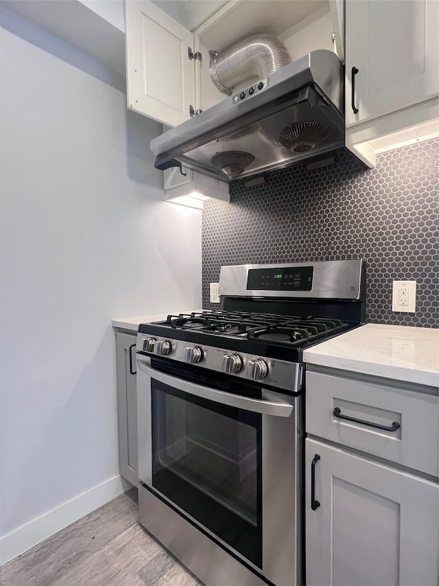 kitchen with stainless steel gas stove, light hardwood / wood-style floors, decorative backsplash, and extractor fan