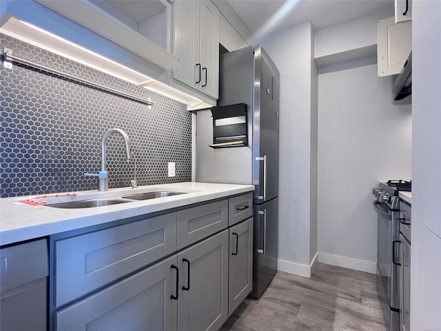 kitchen featuring gray cabinetry, black range oven, sink, tasteful backsplash, and light hardwood / wood-style floors