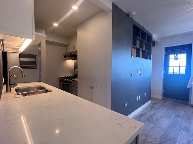 kitchen with hardwood / wood-style floors, sink, gas range oven, light stone counters, and white cabinetry