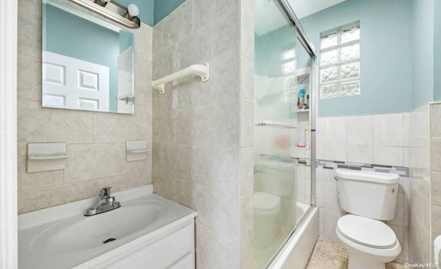 full bathroom featuring toilet, vanity, tile walls, and combined bath / shower with glass door