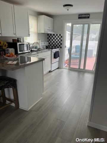 kitchen featuring white cabinets, sink, light hardwood / wood-style flooring, white electric range oven, and a breakfast bar area