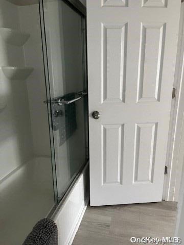 bathroom featuring wood-type flooring and combined bath / shower with glass door