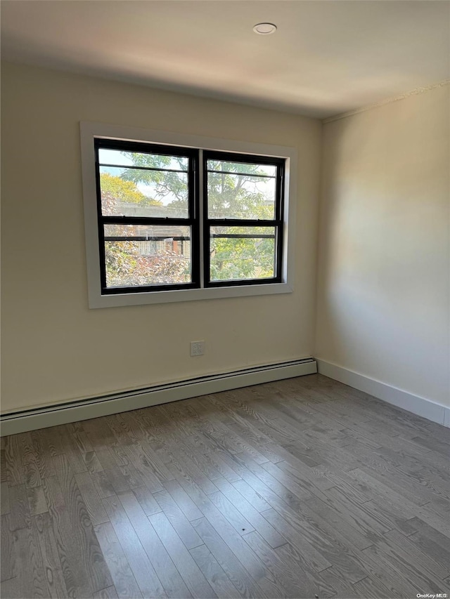 unfurnished room with plenty of natural light, light hardwood / wood-style floors, and a baseboard heating unit