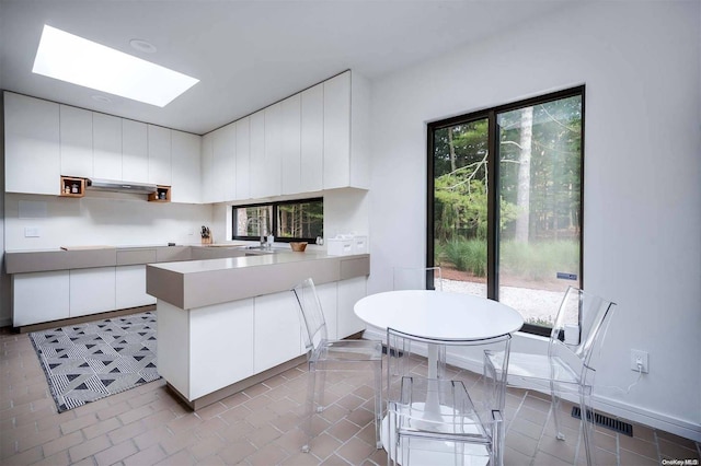 kitchen with exhaust hood, white cabinets, sink, a skylight, and kitchen peninsula