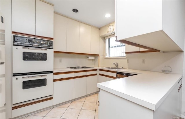 kitchen with kitchen peninsula, white appliances, sink, light tile patterned floors, and white cabinetry