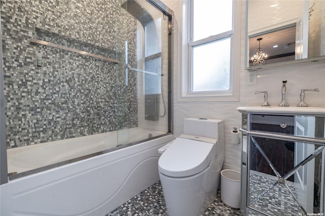 bathroom featuring an inviting chandelier, bath / shower combo with glass door, tile walls, and toilet