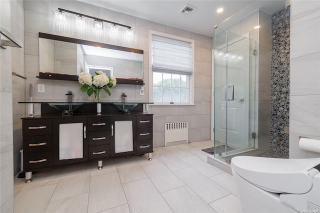 bathroom with radiator heating unit, tile patterned floors, vanity, a shower with shower door, and tile walls