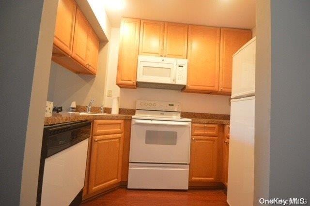 kitchen with sink, dark wood-type flooring, white appliances, and light brown cabinets