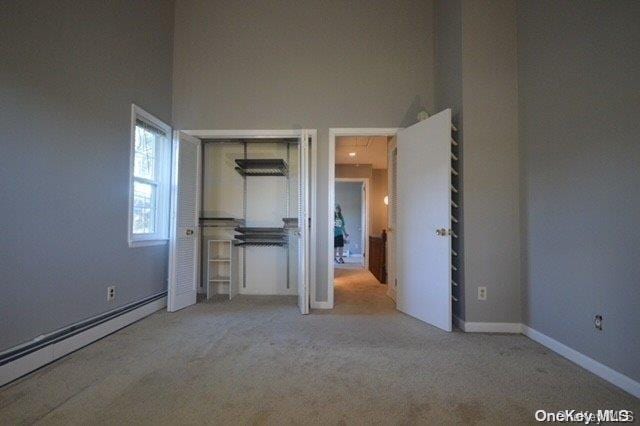 interior space featuring light carpet, a towering ceiling, and baseboard heating