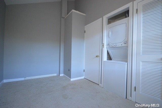 clothes washing area with light colored carpet and stacked washer / drying machine