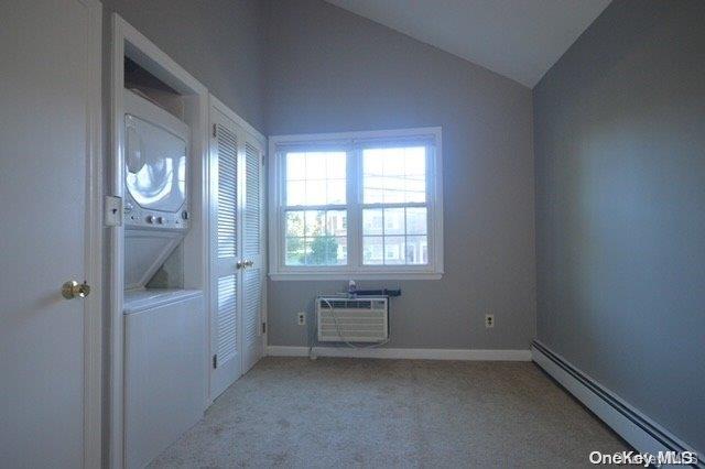 carpeted empty room featuring an AC wall unit, a baseboard radiator, and vaulted ceiling