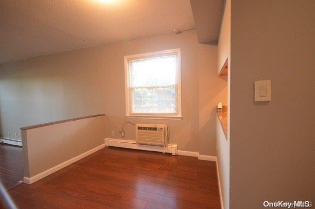 additional living space with a textured ceiling, a baseboard radiator, a wall mounted AC, and dark wood-type flooring