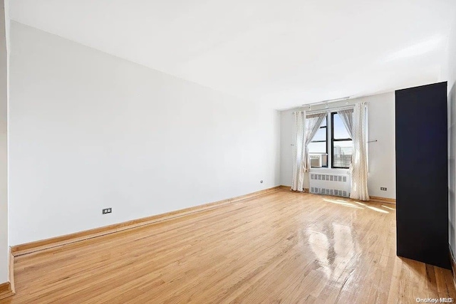 empty room with cooling unit, radiator heating unit, and light hardwood / wood-style flooring