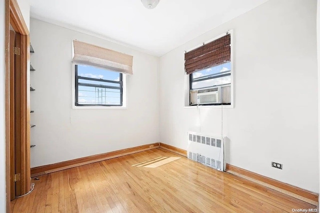 unfurnished room featuring hardwood / wood-style floors, cooling unit, and radiator heating unit