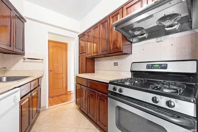 kitchen featuring sink, stainless steel gas range oven, white dishwasher, light tile patterned floors, and exhaust hood