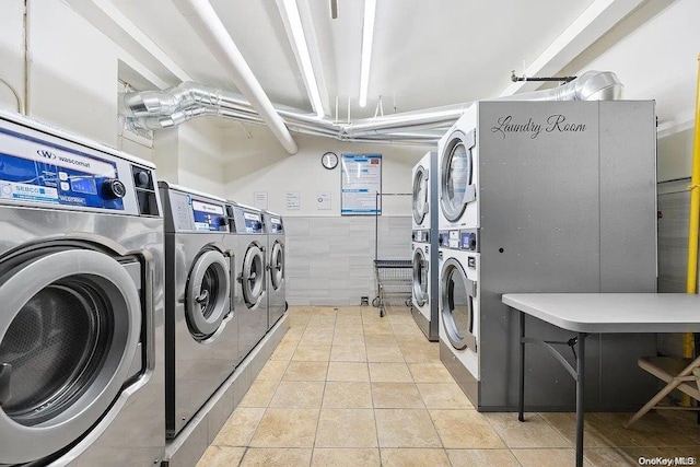 clothes washing area with stacked washer / dryer, light tile patterned floors, washer and dryer, and tile walls