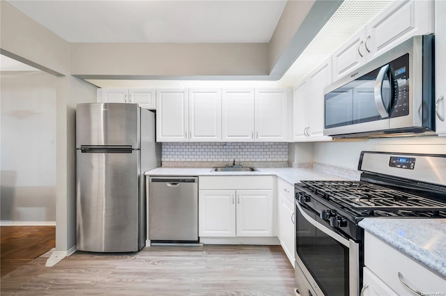 kitchen featuring white cabinets, light wood-type flooring, stainless steel appliances, and backsplash