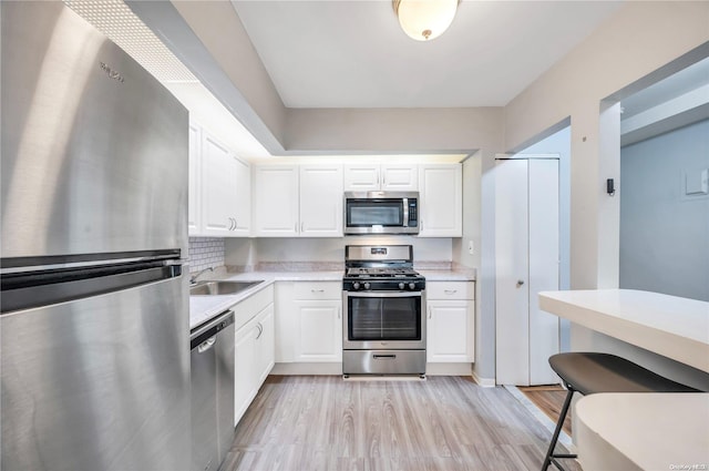 kitchen featuring sink, light hardwood / wood-style flooring, decorative backsplash, white cabinets, and appliances with stainless steel finishes