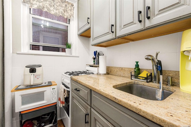 kitchen featuring light stone countertops, gas range, tasteful backsplash, and sink