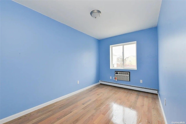 spare room with a baseboard radiator, an AC wall unit, and light hardwood / wood-style floors