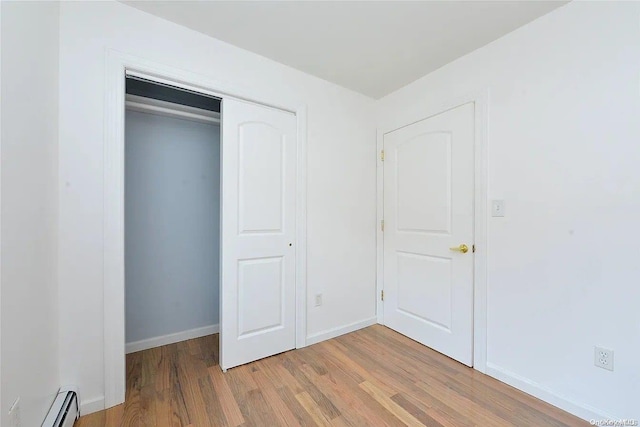 unfurnished bedroom with a closet, light hardwood / wood-style floors, and a baseboard heating unit