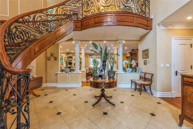 entryway featuring a towering ceiling, light hardwood / wood-style flooring, ornate columns, and ornamental molding