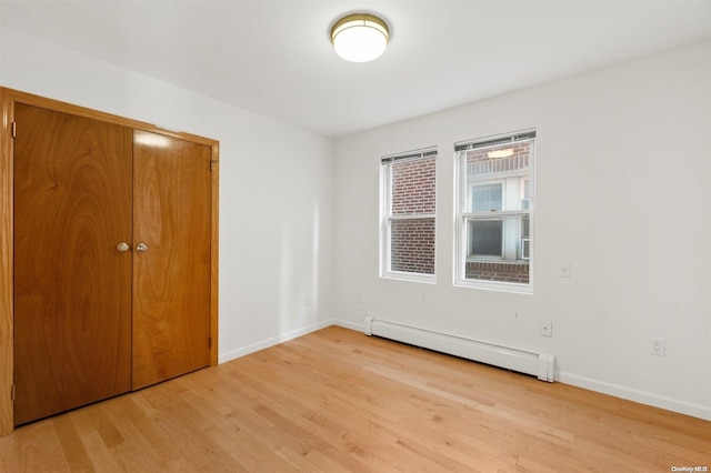 unfurnished bedroom featuring a closet, light hardwood / wood-style flooring, and a baseboard heating unit