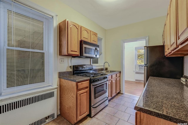 kitchen featuring light tile patterned flooring, appliances with stainless steel finishes, radiator heating unit, and sink